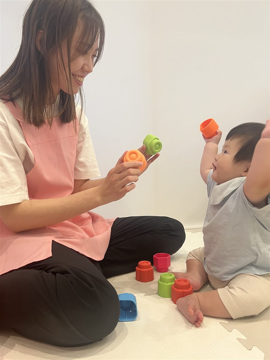 保育士がお子さまと向かい合い、カラフルなおもちゃで一緒に遊んでいる様子